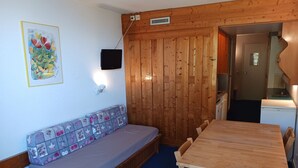 A room with a wooden wall, a bench with patterned cushions, a wooden table, and a television mounted on the wall.