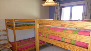 A bunk bed room with a wooden frame, a chair, and a window with curtains.