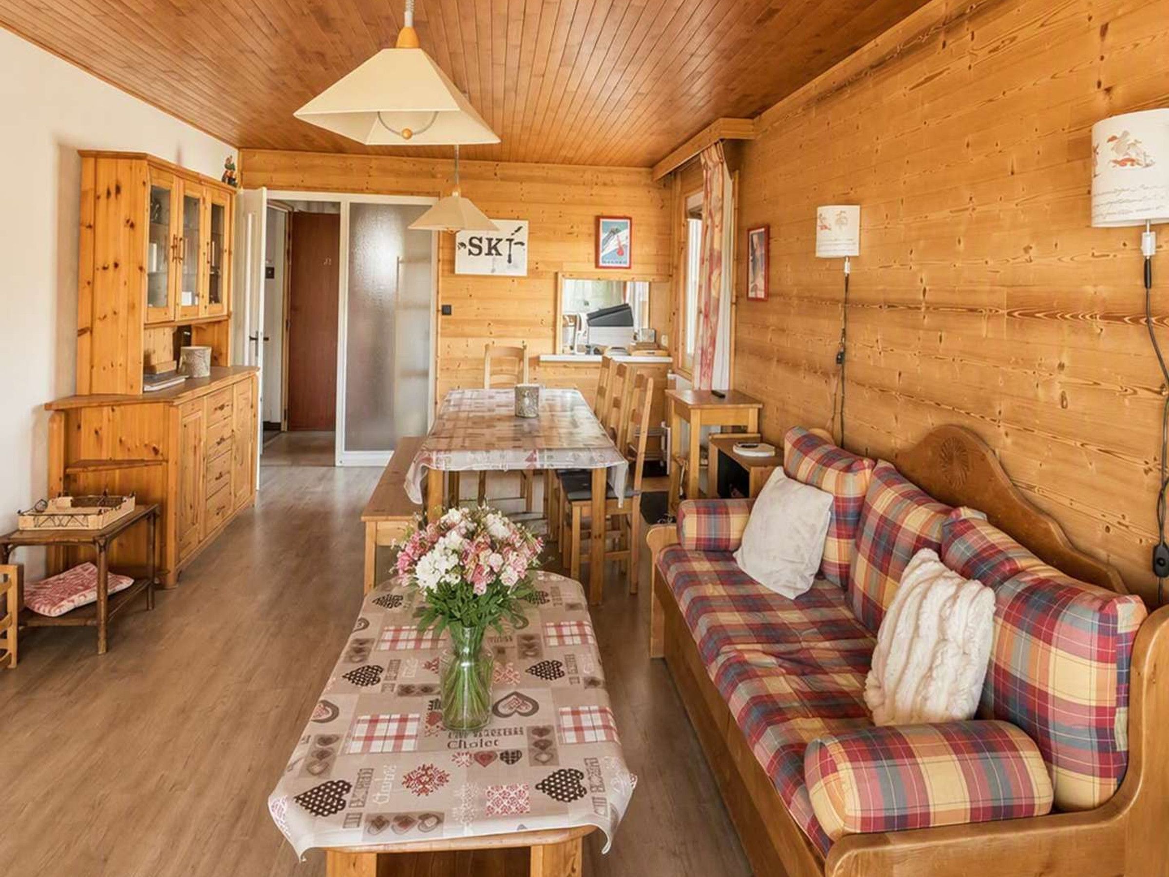 A cozy cabin interior with a dining table, sofa, wooden cabinets, and a ski sign.