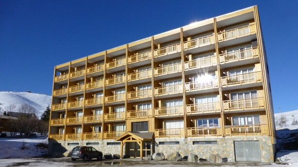 A multi-story hotel with balconies, a covered entrance, and a parking area.