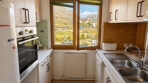 A compact kitchen with white cabinets, a built-in oven, a sink, and a window with a view of a town and mountains.
