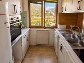 A compact kitchen with white cabinetry, a built-in oven, a sink, and a window with a view of a town and mountains. - Cozy 3P6P apartment near slopes in L'Alpe d'Huez (Huez)