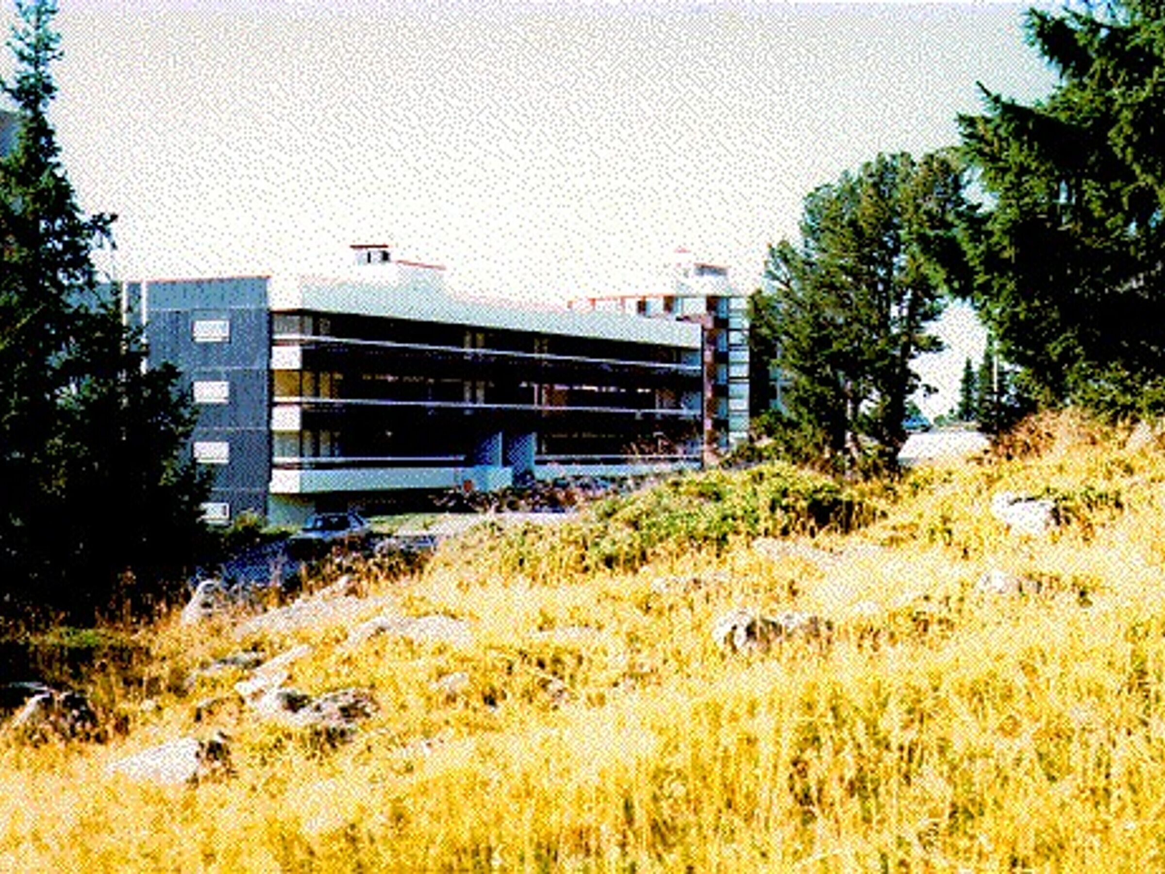 Een modern gebouw met een plat dak en meerdere balkons, omgeven door natuur en bomen.