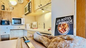 A kitchen with wooden cabinets, a microwave, a kettle, and a bread loaf on a cutting board. - 2-room apartment, 6 ppl, Tignes, near slopes and shops (Tignes)