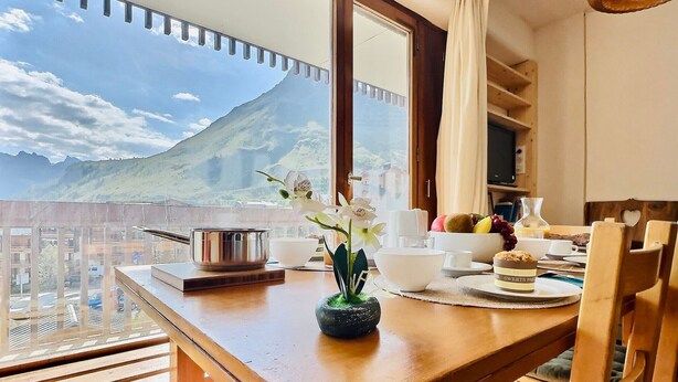 A balcony with a view of a mountain, a wooden table with a vase of flowers, and a breakfast setting. - 2-room apartment, 6 ppl, Tignes, near slopes and shops (Tignes)