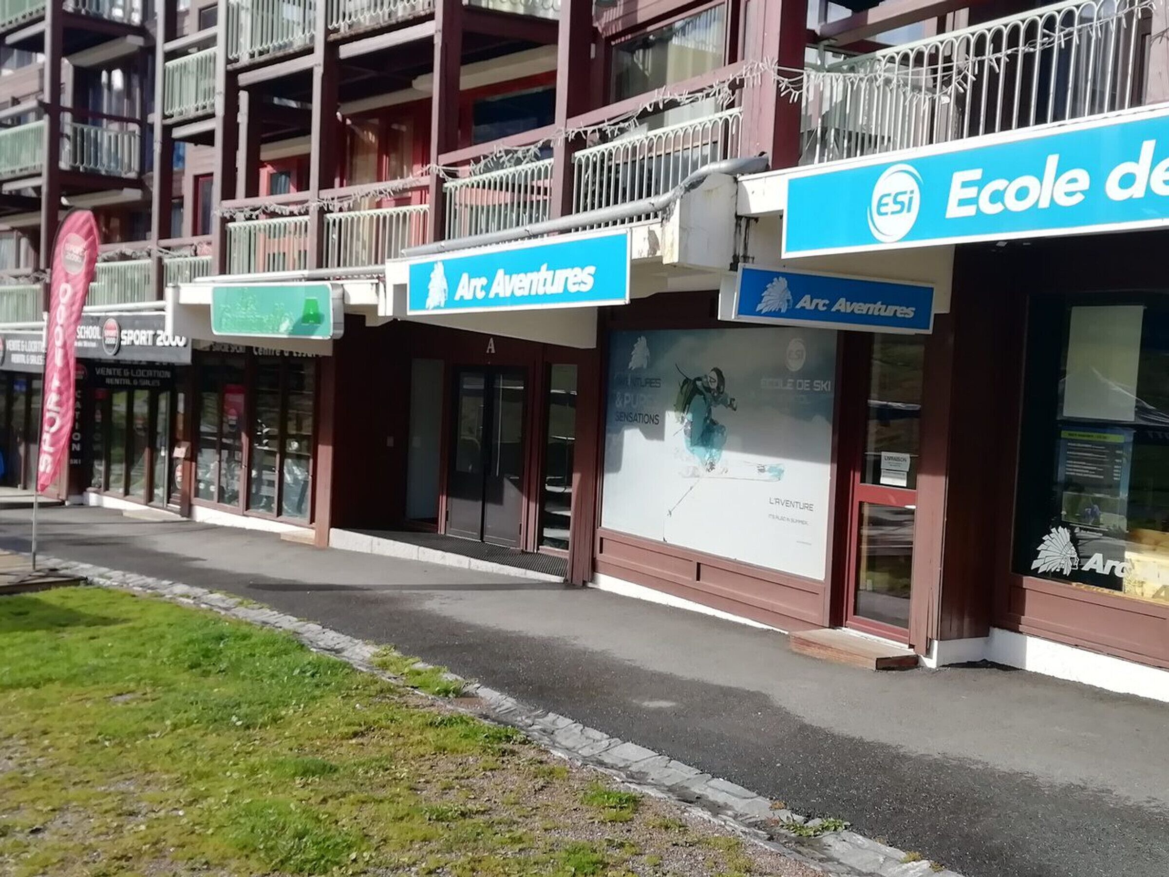 Un immeuble abritant plusieurs commerces, notamment « Arc Adventures » et « École de ski ».