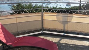 A balcony with a red chair, a view of a marina with boats, and a distant shoreline. - Architect-designed house in Ploumanac'h with stunning sea view (Perros-Guirec)