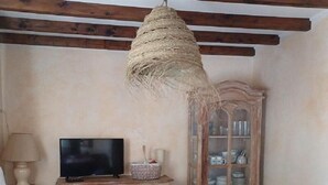 A cozy living room with a television on a wooden cabinet, a hanging light fixture, and a cabinet with glass doors. - Leï Bugadiero - LA CROIX VALMER (La Croix-Valmer)