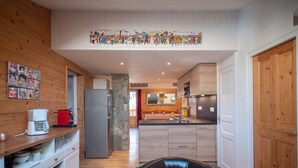A modern kitchen with wooden walls, a stone column, a black leather chair, and a festive banner. - Spacious apartment in Valmorel, 11 beds, 4 rooms, ski locker (Valmorel)