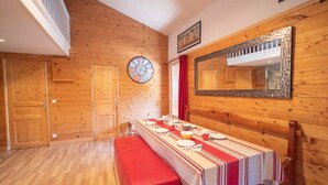A wooden-paneled room with a dining table set for four, a clock, and a mirror on the wall. - Spacious apartment in Valmorel, 11 beds, 4 rooms, ski locker (Valmorel)