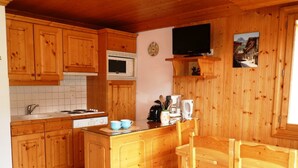 A wooden kitchen with a central island, a microwave, a stove, and a television mounted on the wall.