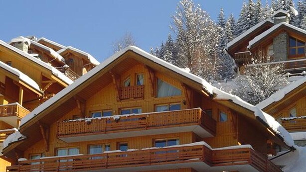 A multi-story wooden chalet with balconies, surrounded by snow-covered trees.