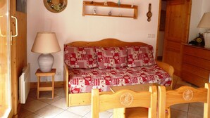 A cozy room with a wooden bed, a small table with a lamp, a shelf with decorative items, and a wooden door.