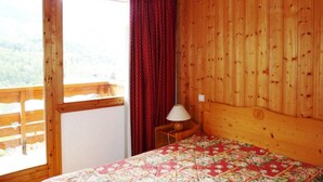 A wooden-paneled room with a bed, a window, and a view of a balcony.