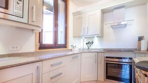 A modern kitchen with white cabinets, a built-in oven, and a window with blinds.