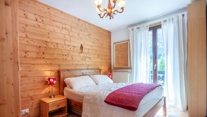 A bedroom with a wooden wall, a bed with white bedding and a red throw, a nightstand with a lamp, and a window with curtains.