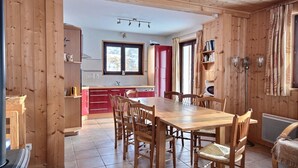 Interior de fusta amb taula de dinar, caires, zona de cuina amb nevera vermella i finestra amb vistes.