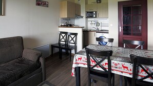 Un espace de vie compact comprenant un canapé, une table à manger, des chaises, un coin cuisine et une porte rouge.
