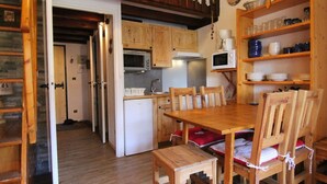 Une cuisine compacte avec des meubles en bois, un four à micro-ondes et un réfrigérateur. On y trouve une table à manger avec des chaises et un petit tabouret en bois.