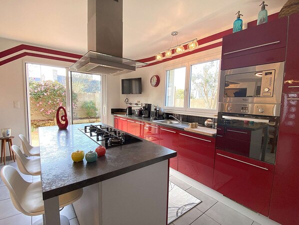 A modern kitchen with red cabinets, a central island, and a large window providing natural light.