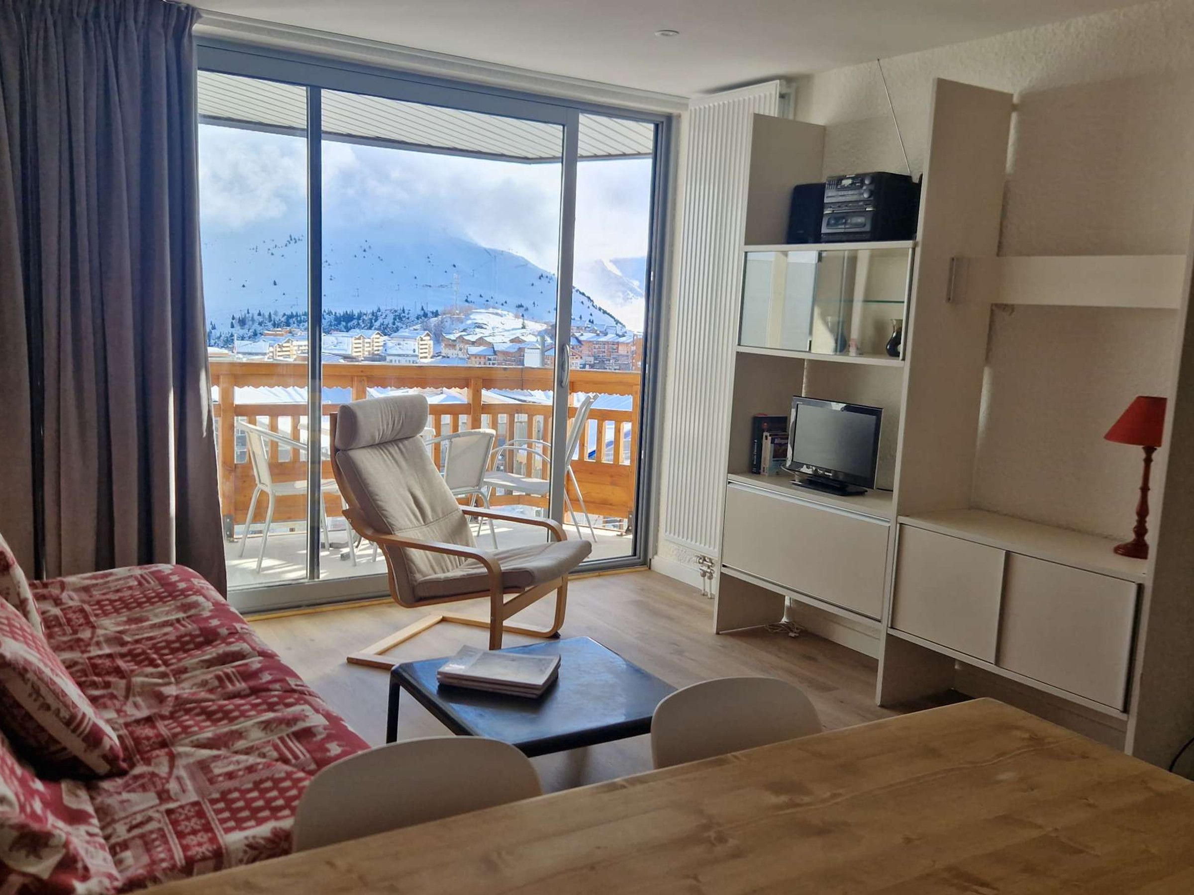 A room with a balcony, a sofa, a chair, a TV, and a lamp.