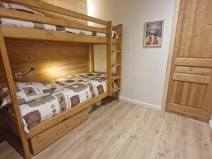 Un lit superposé avec une couvre-lit à motifs, une armoire en bois et une porte ornée d’une affiche.