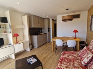 Un espace de vie compact comprenant un coin cuisine, un coin repas et un canapé agrémenté de coussins à motifs.