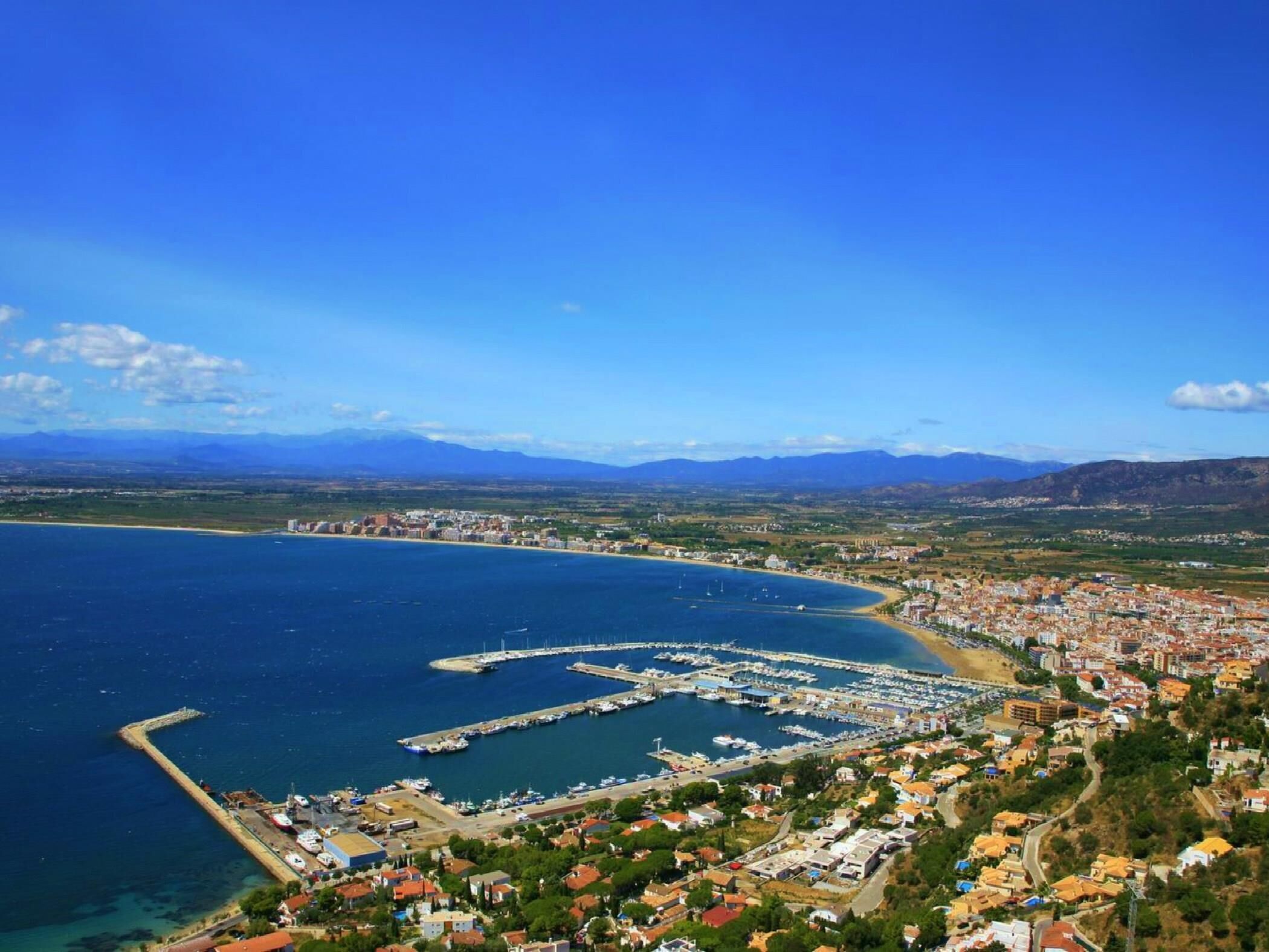 A coastal town with a marina, residential buildings, and a mountainous backdrop.