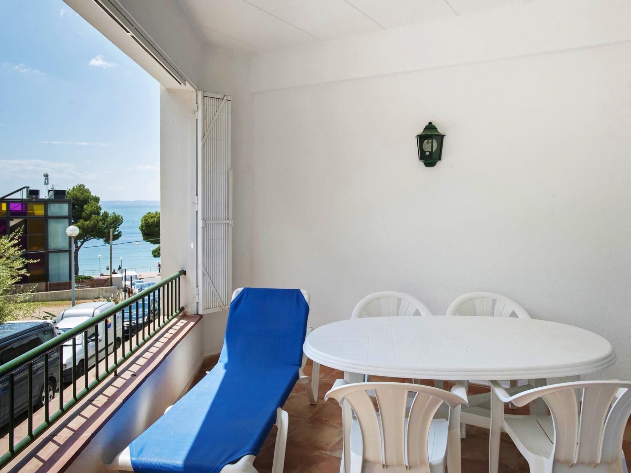 Un balcon avec une chaise bleue, une table blanche et d’autres chaises, donnant sur une étendue d’eau et des bâtiments.