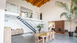 Amplia sala de estar con una mesa de comedor, sillas, una escalera y una planta grande en maceta.