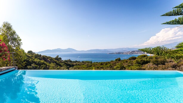 Una piscina azul cristalina con vistas al mar y montañas al fondo.