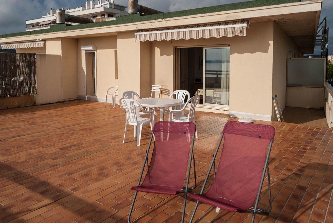 A rooftop terrace with a wooden floor, white plastic chairs, and a table.