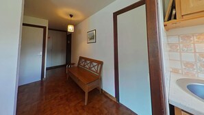 Un pasillo con suelo de madera, un banco, una lámpara colgante y una zona de cocina con azulejos.