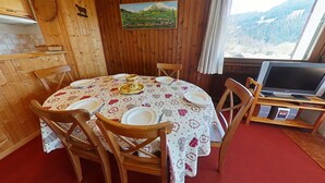 Un comedor acogedor con una mesa redonda para cuatro personas, sillas de madera, un cuadro de un paisaje y un televisor sobre un mueble de madera.