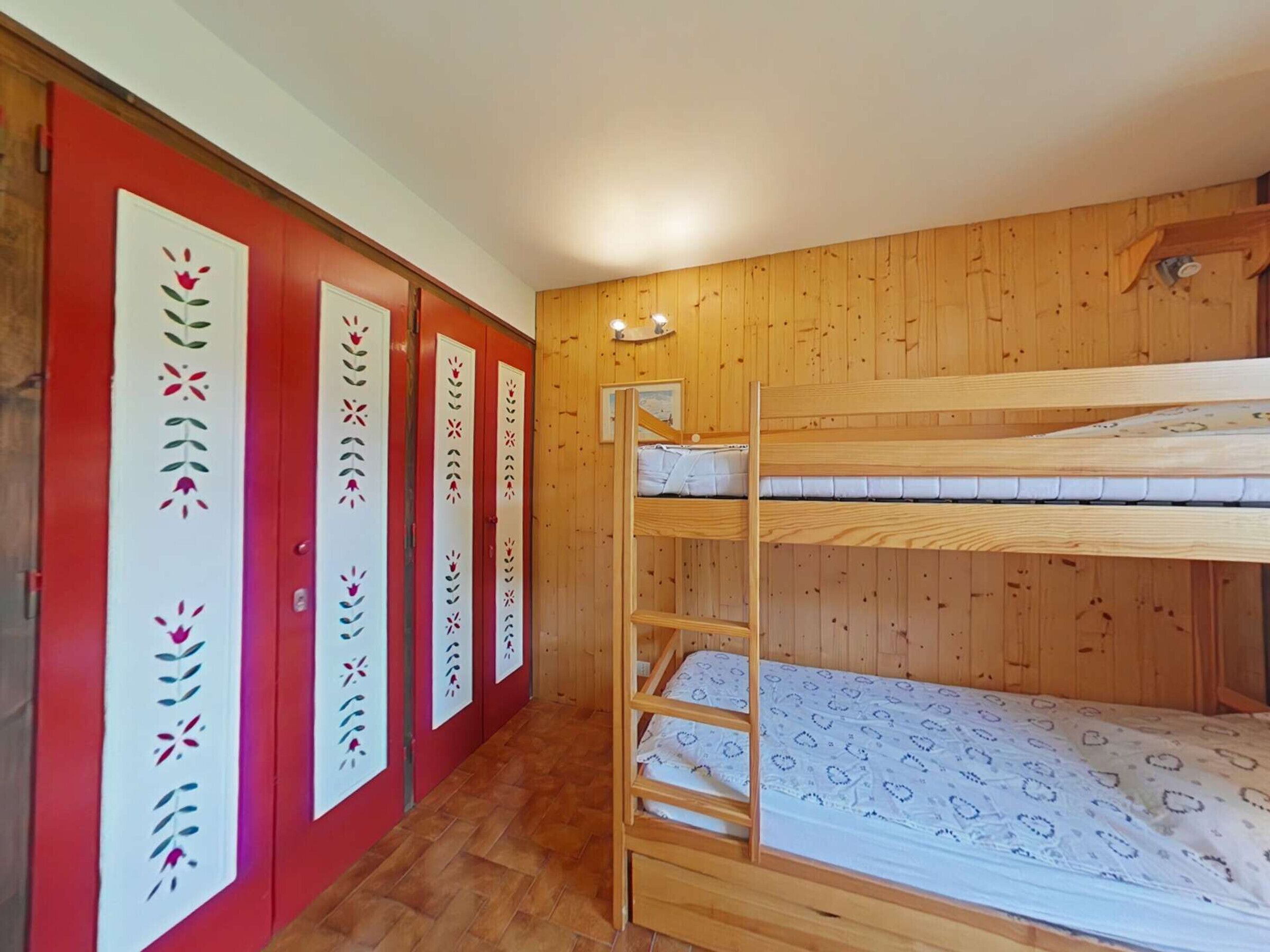 Een slaapkamer met stapelbedden, houten wanden en een rode deur.