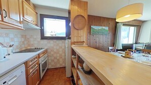 Una cocina compacta con armarios de madera, salpicadero azulejado, ventana y una mesa de comedor de madera con sillas.
