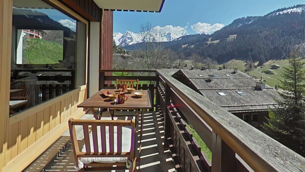 Un balcón con mesa y sillas, con vistas a un paisaje montañoso con picos nevados.