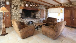 A rustic living room with stone walls, wooden beams, a fireplace, and leather armchairs. - Cozy Cottage with Fireplace, Garden, and Game Room near the Sea (La Hague)