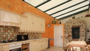A kitchen with a stone wall, a wooden table, and a tiled backsplash. - Cozy Cottage with Fireplace, Garden, and Game Room near the Sea (La Hague)