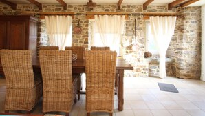 A dining area with wicker chairs, a wooden table, stone walls, and a stone fireplace. - Cozy Cottage with Fireplace, Garden, and Game Room near the Sea (La Hague)