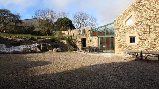 A stone building with a glass extension, outdoor seating, and a gravel area. - Cozy Cottage with Fireplace, Garden, and Game Room near the Sea (La Hague)