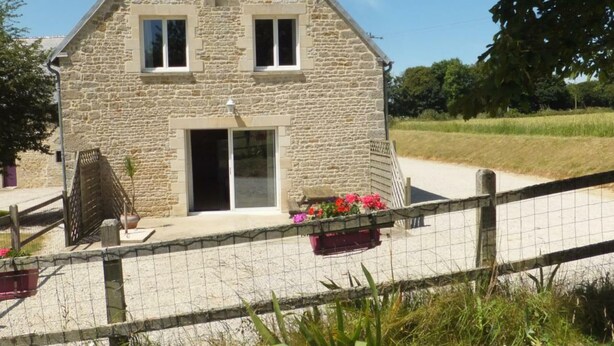 Una casa in pietra con tetto spiovente, una porta d'ingresso e un piccolo portico con piante in vaso.