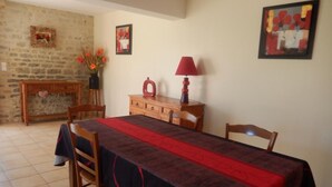 Zona pranzo con tavolo imbandito per quattro persone, un mobiletto in legno, un vaso con fiori e due quadri appesi al muro.