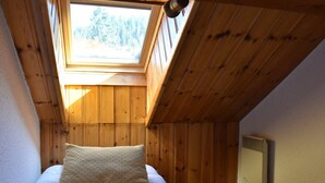 Camera da letto con soffitto spiovente, pareti in legno, un lucernario, un letto con biancheria bianca e un termosifone a parete.