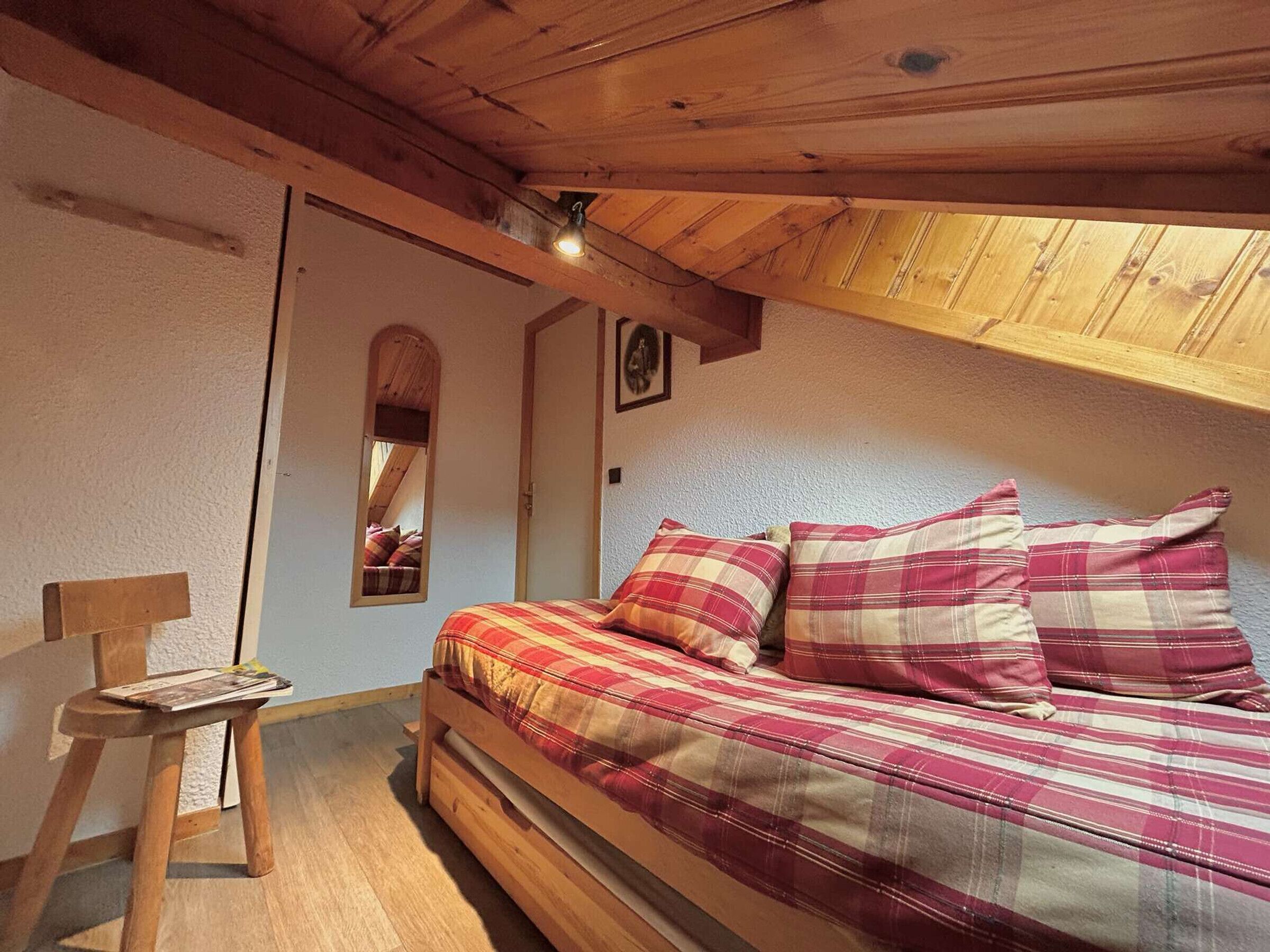 Um quarto acolhedor com uma cama de madeira, uma pequena cadeira de madeira, um espelho e um teto inclinado.