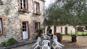 Un bâtiment en pierre doté d’une terrasse en gravier, d’un espace extérieur aménagé pour s’asseoir et d’un coin barbecue.