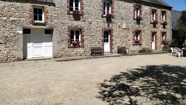 Un bâtiment en pierre avec une porte blanche, de nombreuses fenêtres ornées de jardinières et des sièges à l’extérieur.