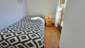 Une chambre à coucher avec une couvre-lit à motifs, une table de chevet avec une lampe et une fenêtre avec des rideaux.