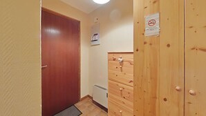 Un couloir avec une porte en bois, un radiateur et un placard sur lequel est apposé un panneau « interdiction de fumer ».