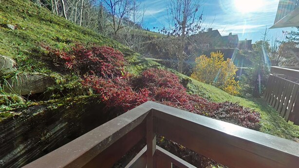 Une vue depuis un balcon doté d’une balustrade, donnant sur un jardin aménagé avec différents arbustes et arbres.